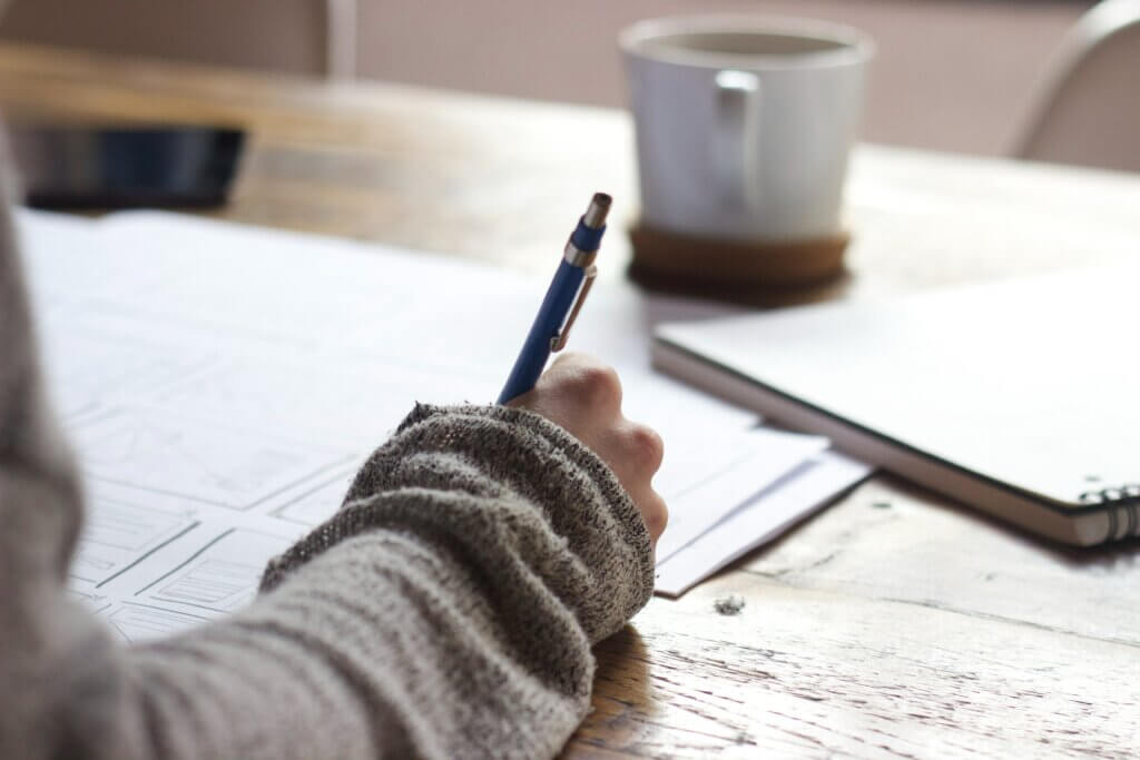 Picture shows a hand with a pen and paper writing a CV for teaching vacancies